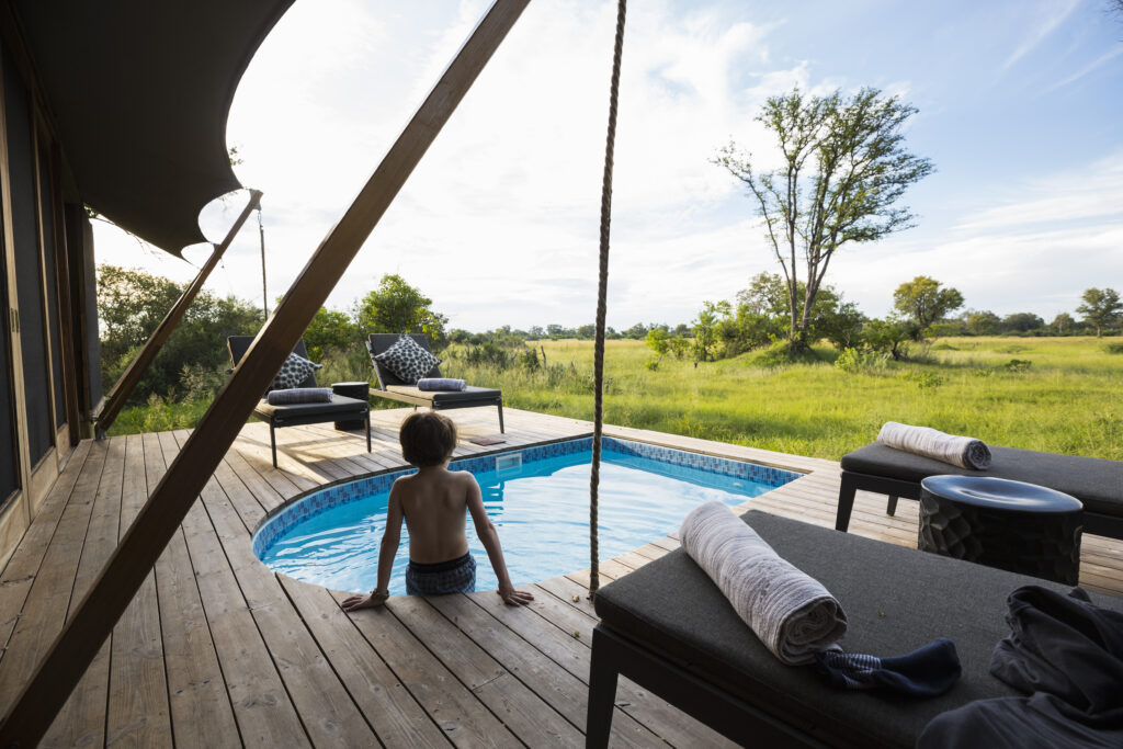 A boy in a swimming pool at a safari camp, looking out over the landscape