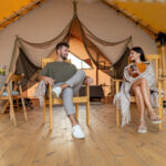 Young relaxed couple having talk while sitting in armchairs on patio of camping tent