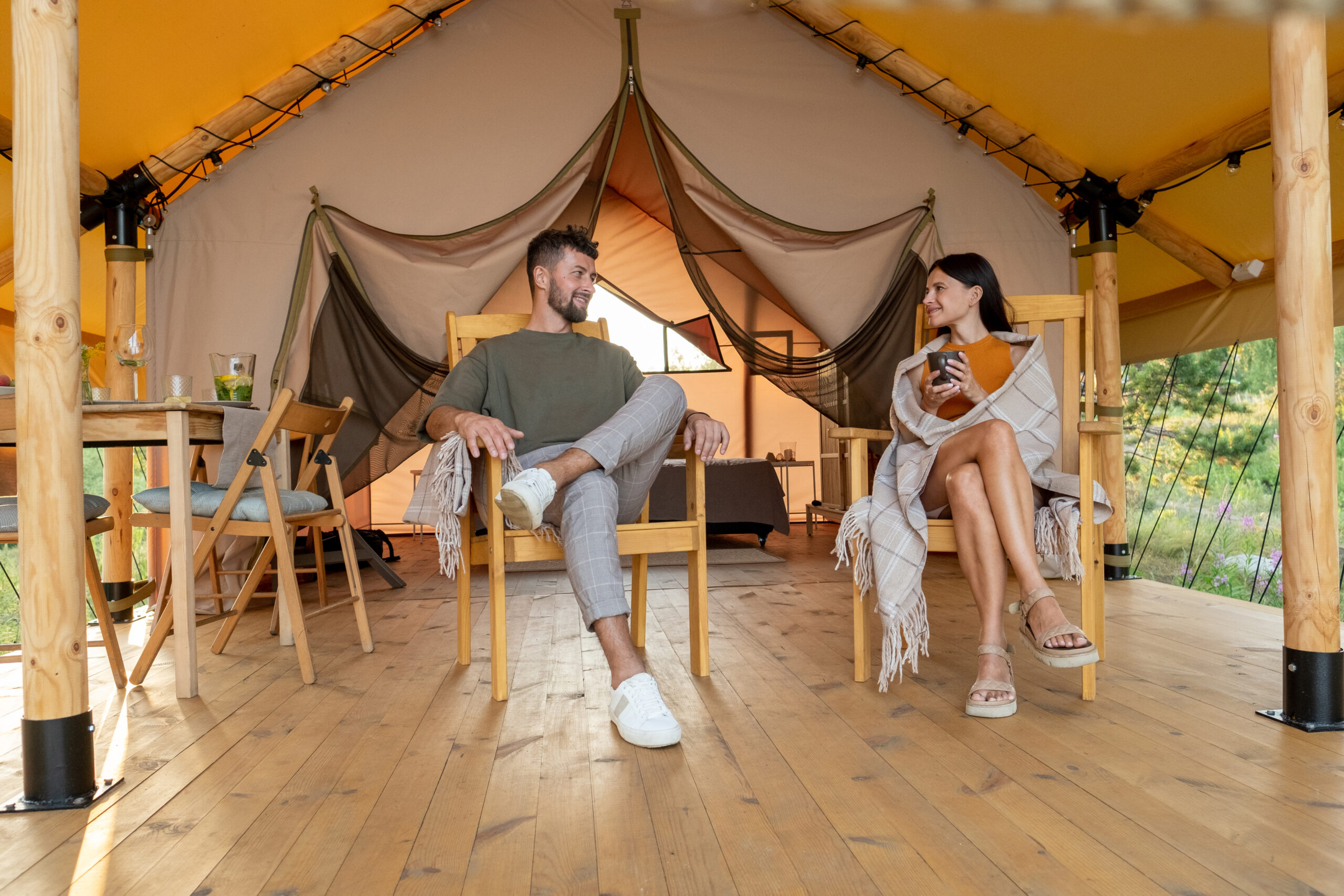 Young relaxed couple having talk while sitting in armchairs on patio of camping tent